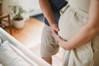 From above of crop faceless couple in casual outfit standing in light living room and touching pregnant belly gently